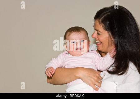 Horizontale close-up-Porträt von einem Kichern sechs Monate altes Babymädchen mit einer Umarmung und längerem "eins zu eins" mit der stolzen Mutter Stockfoto