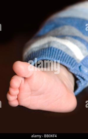 Vertikale Nahaufnahme Portrait eines Neugeborenen s perfekte kleine Fußes vor schwarzem Hintergrund Stockfoto