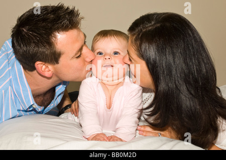 Horizontale Nahaufnahme Portrait ein sechs Monate altes Baby und Eltern stolz auf die Wange küssen Stockfoto