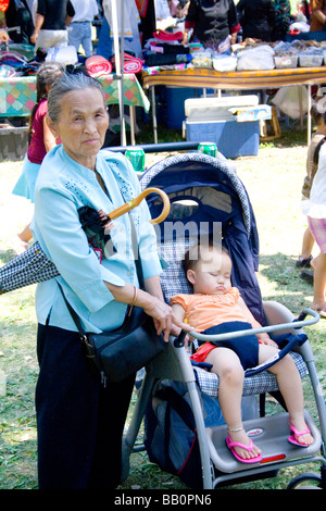 Ältere Hmong asiatischen Großmutter zu wachen über Baby im Kinderwagen. Hmong Sport Festival McMurray Feld St Paul Minnesota USA Stockfoto