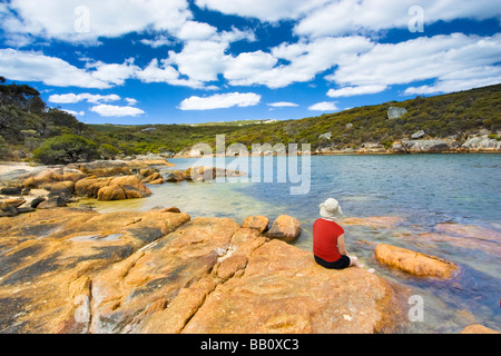 Eine junge Frau saß auf Granitfelsen neben dem Waychinicup Fluss Einlass im Waychinicup National Park in der Nähe von Albany, Westaustralien Stockfoto