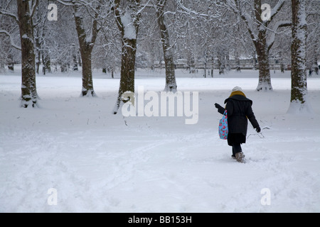 Frau zu Fuß zur Arbeit durch den tief verschneiten Park, London Stockfoto