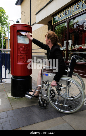 Weibliche Rollstuhlfahrer buchen einen Brief in einen Briefkasten der Royal Mail Stockfoto