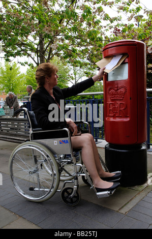 Weibliche Rollstuhlfahrer buchen einen Brief in einen Briefkasten der Royal Mail Stockfoto