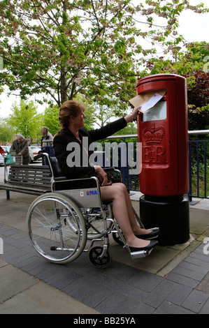 Weibliche Rollstuhlfahrer buchen einen Brief in einen Briefkasten der Royal Mail Stockfoto