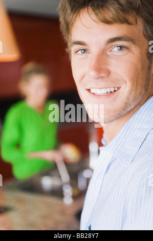Porträt eines Mannes mit einer Frau waschen Gemüse im Hintergrund lächelt Stockfoto