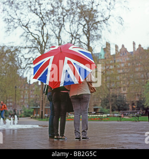 Touristen, die sich vor dem Regen unter einem Schirm der Union Jack Flagge in Russell Square, Bloomsbury London England Großbritannien schützen. KATHY DEWITT Stockfoto