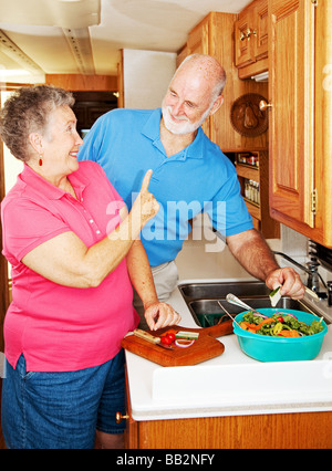 Ältere Dame spielerisch Schelte ihres Mannes für reißt eine Gurke aus dem Salat macht Sie Stockfoto