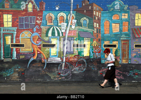 Eine Frau, die zu Fuß auf dem Bürgersteig Vergangenheit ein Graffiti in der Garage nebenan, in der Innenstadt von Toronto, Ontario, Kanada. Stockfoto