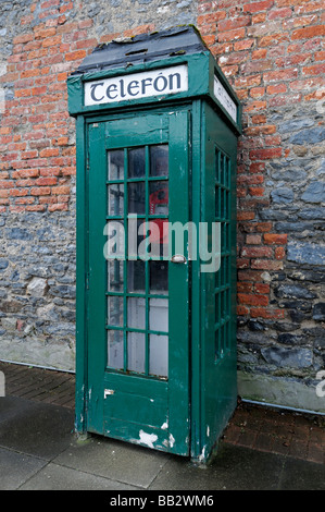 Traditionelle irische grüne Telefon Box geschlossen Tür vor rotem Backstein Wand alte unbenutzte stillgelegten Baufälligkeit veraltet Technologie Stockfoto