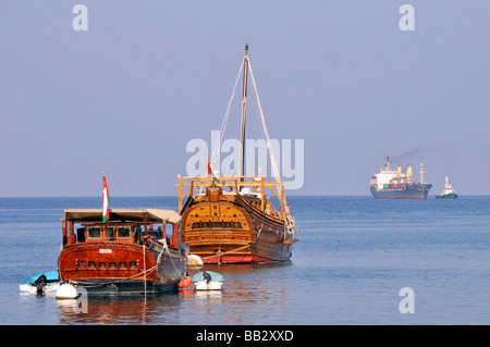 Antikes und modernes Schiff in Port Sultan Qaboos Muscat Oman dhows im Hafen von Muttrah festgemacht Schlepper Containerschiff in Richtung Port Golf von Oman Stockfoto