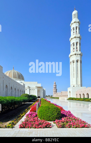 Minarett in atemberaubendem Außenblick auf weiße religiöse Gebäude und Blumen in der Sultan Qaboos Grand Moschee am blauen Himmelstag Muscat Oman Mittlerer Osten Asien Stockfoto