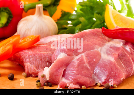 Frisches rohes Schweinefleisch an Bord mit Gemüse, Paprika, Knoblauch, Parslay, Zitrone und Gewürzen Stockfoto