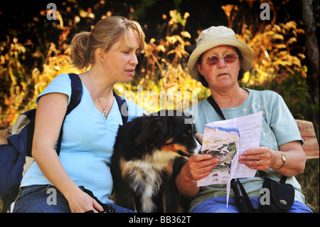 Zwei Frauen Wanderer sitzt auf einer Holzbank, eine Pause, mit ihrem Hund zwischen ihnen. Stockfoto