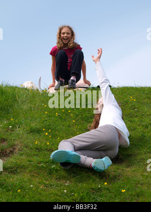 Zwei junge Mädchen, die Spaß einen grasbewachsenen Hügel hinunter gleiten Stockfoto