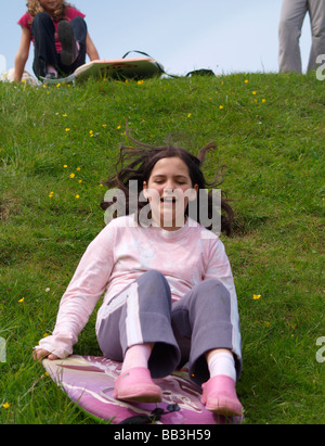 Junges Mädchen rutscht einem grasbewachsenen Hügel auf einem bodyboard Stockfoto