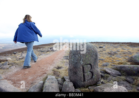 Walker den Weg vom Gipfel des Mount Keen in Glen Esk absteigend, übergibt Angus, Schottland, UK, einen alten Grenzstein Stockfoto