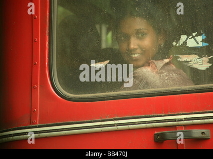 Ein Junge srilankischen Frau lächelt durch die Heckscheibe des roten Busses reitet sie auf.  Kandy, Sri Lanka Stockfoto