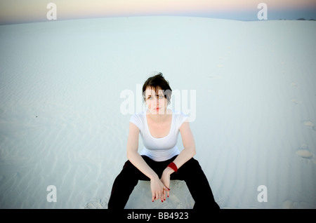 Eine junge Frau starrt auf meine Kamera beim Sitzen auf einer Sanddüne am White Sands National Monument. Stockfoto