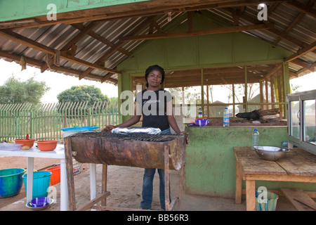 Eine junge Frau grillt Fisch an einem Straßenrand "point and kill" Fisch Stand im Millenium Park in Abuja, Nigeria. Stockfoto