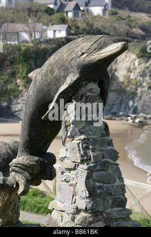 Dorf von Aberporth, Wales. Paul Clarke gestaltet springenden Delfin Schnitzen mit Aberporth Weststrand im Hintergrund. Stockfoto