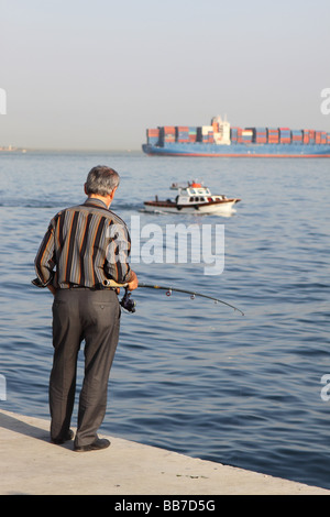 Istanbul Türkei Mann Angeln am Meer in Kumkapi mit großen Containerschiff Schiff hinter den Bosporus verlassen Stockfoto