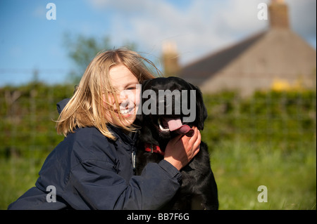 Lächelnde blondes Mädchen umarmt Labrador Hund auf einer Wiese Cumbria Stockfoto