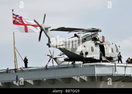 Hubschrauber wird über Deck der HMS Illustrious Licht Flugzeugträger mit White Ensign Fahne manövriert Stockfoto