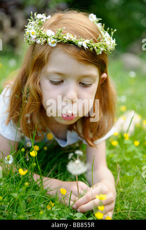 Junge Mädchen tragen einen Blumenkranz im Haar weht eine Löwenzahn Uhr Stockfoto