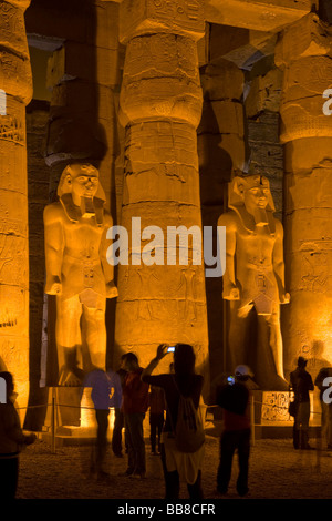 Zwei beleuchtete Statuen von Ramses II, Touristen fotografieren, ersten Innenhof, Luxor-Tempel bei Nacht, Luxor, Ägypten Stockfoto