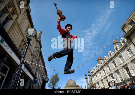 A Street Theatre Straßenmusiker spielt auf einer Violine beim Balancieren auf einem Drahtseil in Brighton Festival Stockfoto