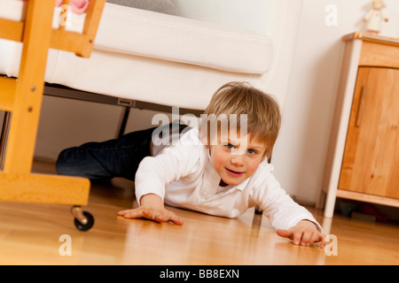 Junge, 6 Jahre alt, liegend auf dem Boden unter einem Sessel Stockfoto