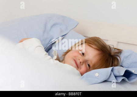 Kleiner Junge, 3 Jahre alt, im Bett zwischen Kissen liegend Stockfoto