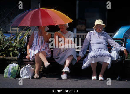 Drei Damen sitzen auf einer Bank im Schatten von der heißen Sommersonne. Worthing. West Sussex Südengland GB. UK Stockfoto