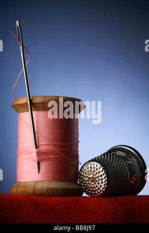 eine hölzerne Spule rosa Faden mit der Nadel stecken und einen Fingerhut Stockfoto
