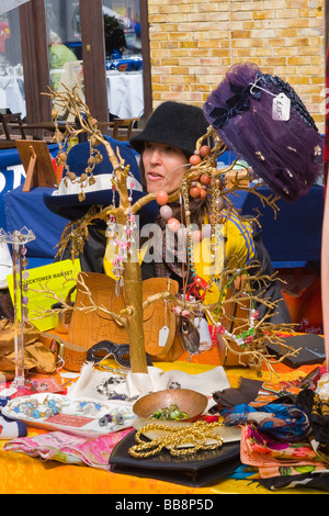 London-Greenwich-Antiquitäten oder Dorf Markt, sitzen mittlere gealterte Dame mit Hut auf Stall mit Hüte Perlen Halsketten etc. Stockfoto