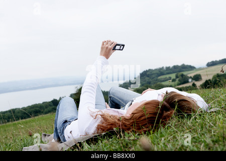 Zwei Jugendliche liegen auf einem Feld fotografieren sich mit Blick auf den See Stockfoto