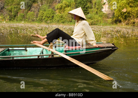 Frau Rudern ihr Boot mit ihren Füßen auf dem Ngo Dong Fluss bei Tam Coc in der Nähe von Ninh Binh Vietnam Stockfoto