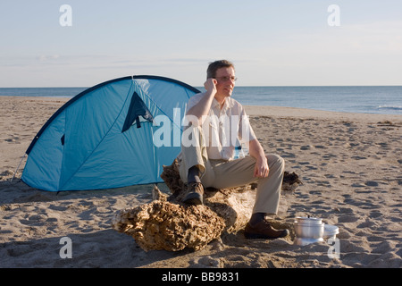 Man sitzt vor seinem Zelt am Strand beim Tätigen eines Anrufs Stockfoto