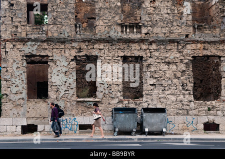 Fußgänger vorbei an einem Haus mit Sprengsätzen Schäden des Krieges 1992-95 in der Stadt Mostar in Bosnien und Herzegowina Stockfoto