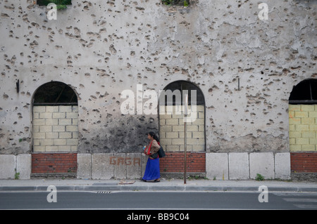Eine Zigeunerin kommt in der Stadt Mostar im Süden von Bosnien und Herzegowina an einem Gebäude vorbei, das mit Einschusslöchern aus dem Krieg von 1992-95 durchlöchert ist Stockfoto