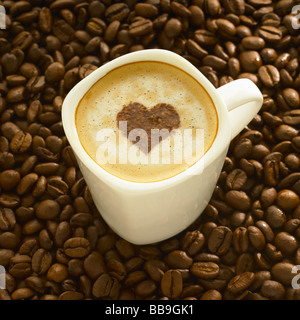 Eine Tasse Kaffee Cappuccino Stil mit einer Herzform auf der Oberseite, geschossen auf Kaffeebohnen. Stockfoto