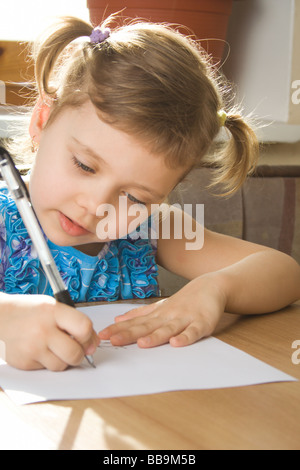 kleines Mädchen lernt schreiben, sitzt an einem Tisch Stockfoto