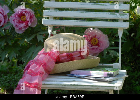 Sonnenhut auf Gartenstuhl vor Pfingstrosen Stockfoto