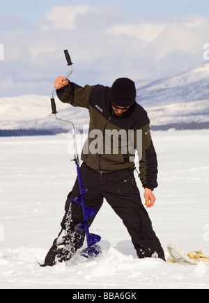 Ismaili Angeln, bohren ein Loch mit einer Eis-Schnecke, Fox Lake, Yukon Territorium, Kanada Stockfoto