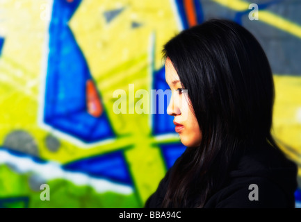 Junge Asiatin in Rapper Pose vor einer Graffitiwand Stockfoto