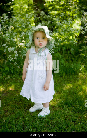 BABY MÄDCHEN KLEINKIND BEI SONNENHUT GENIEßEN SIE SONNENSCHEIN UND BLUMEN IN EINEN ENGLISCHEN GARTEN. Stockfoto