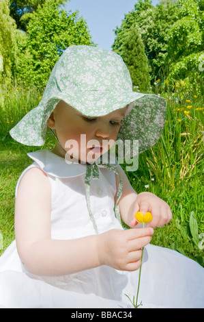 BABY MÄDCHEN KLEINKIND BEI SONNENHUT GENIEßEN SIE SONNENSCHEIN UND BLUMEN IN EINEN ENGLISCHEN GARTEN. Stockfoto