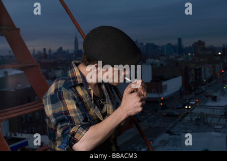 Ein junger Mann stehend auf einer Feuertreppe, zündet sich eine Zigarette Stockfoto