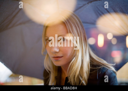 Eine junge Frau hält einen Regenschirm und Blick durch ein Fenster Stockfoto